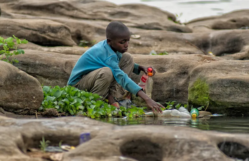 A person collecting plastic bottles from the bank of a river