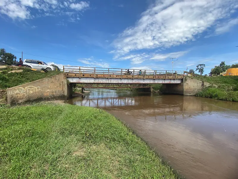 A narrow stretch of the River Rwizi seen from a bridge, bordered by thick riverside vegetation