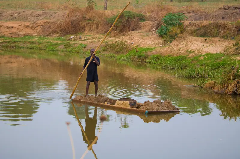 A person digging sand from a dry riverbed with a shovel